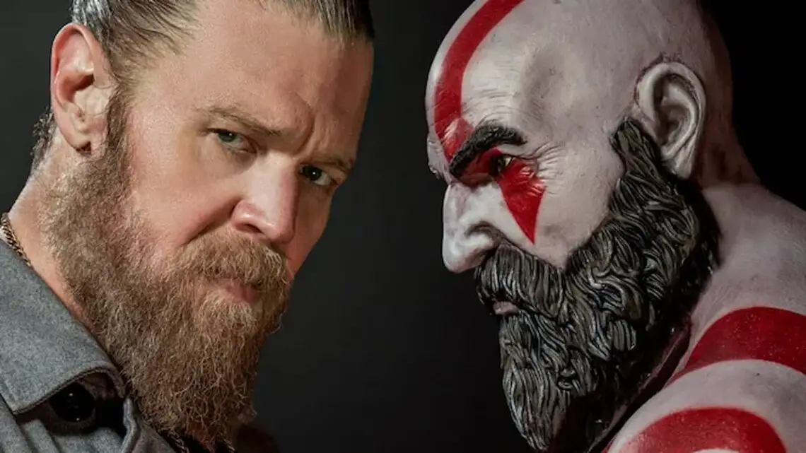 Ryan Hurst looks at the camera next to a statue of Kratos from God of War.