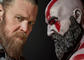 Ryan Hurst looks at the camera next to a statue of Kratos from God of War.