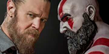 Ryan Hurst looks at the camera next to a statue of Kratos from God of War.